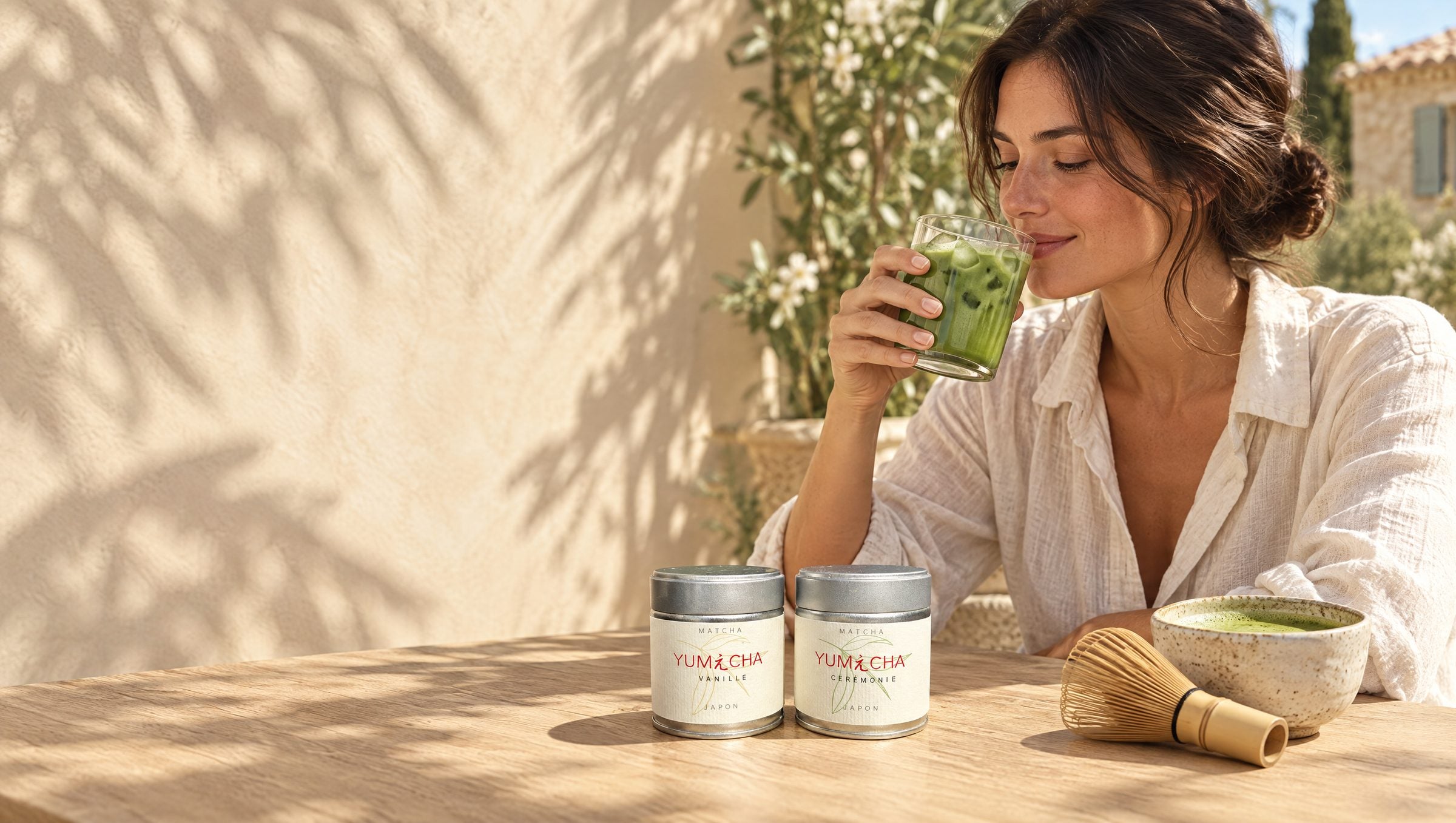 Une femme boit un matcha glacé Yumecha en terrasse, les deux boîtes Cérémonie et Vanille posées sur la table